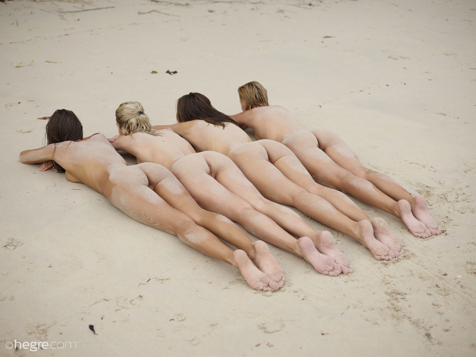Голые девушки лежат на песке попками вверх