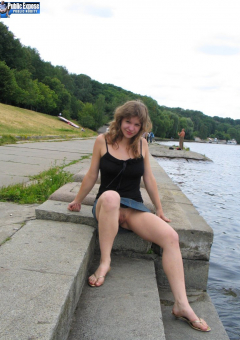 Девушка без трусов сидит на бетонных плитах возле речки